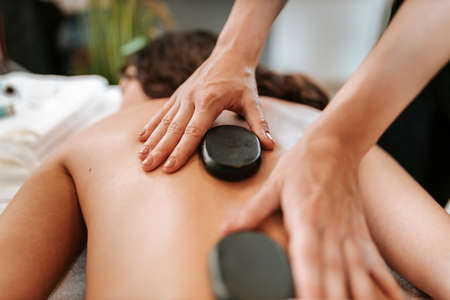 Beauty treatment concept with masseur and her patient. Masseur doing massage on woman body in the spa salon. Beautiful girl with brown curly hair and creol skin having recovery massage.の写真素材