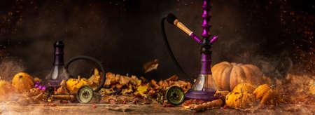 Autumn concept of arabic hookah or shisha with orange pumpkin and dry, colorful leaves of october. Still life shoot with copy space, ideal for text or logoの写真素材