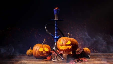 Autumn concept of arabic hookah or shisha with orange pumpkin and dry, colorful leaves of october....