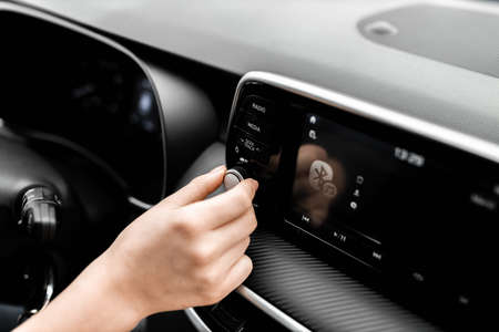 Young woman controls the audio system in the brand new car. Interior view of a car. Synthetic...