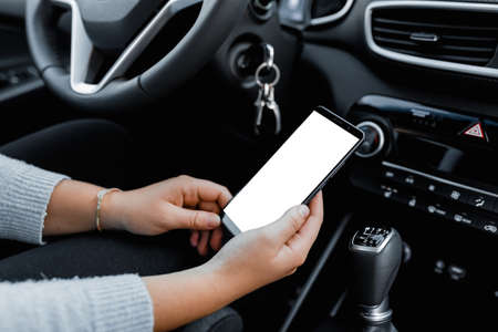 Young driver using smartphon in the car while driving or parking. Mockup of a mobile phone with isolated white screen in the hands of a woman.の写真素材