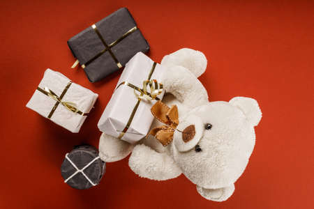 White or light brown adorable teddy bear with christmas decorations and gifts. Holiday concept with toy plush bear and christmass gifts on the red table.の写真素材