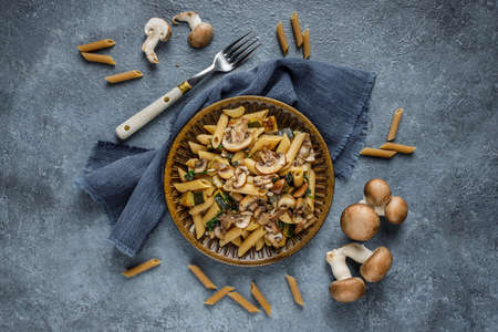 Flat lay photo of pasta penne with roasted mushrooms, garlic and zucchini. Italian food on blue marble table.の写真素材