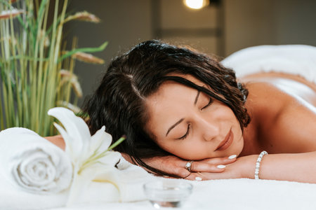 Beauty treatment concept with masseur and her patient. Masseur doing massage on woman body in the spa salon. Beautiful girl with brown curly hair and creol skin having recovery massage.の写真素材