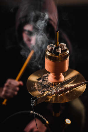 Close up hookah against beardy man. Smoking Shisha in a dark room, white cloud of smoke