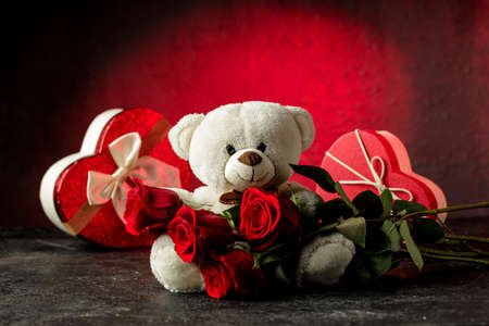 Adorable light brown and white teddy bear with a bouquet of red rose and hearth shaped gift box. Valentines day conceptの写真素材