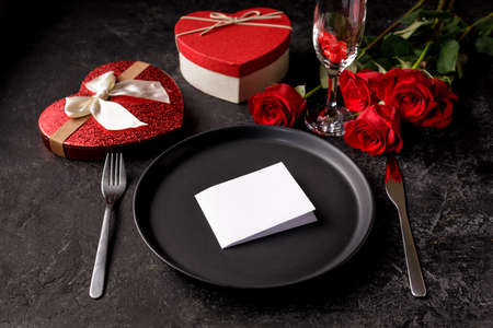 Valentines day or birth day celebration dinner concept with an empty black matte plate, hearth shaped gift box and red rosesの写真素材