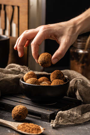 Woman hand take out a peace of homemade delicious cocoa ball with healthy ingredients from a black...