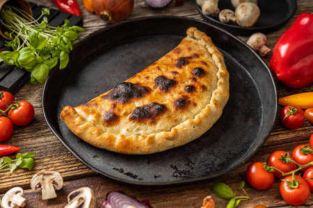 Pizza calzone on a black plate with vegetablesの写真素材