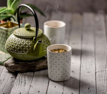 Still life of a cup of tea with a box of herbal tea and a traditional green metal tea pot in the background.の写真素材