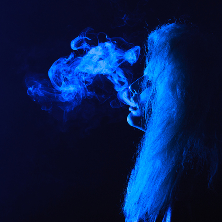 dark and sullen shot of a young woman smoking over a black background