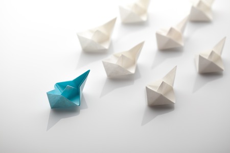 Leadership concept using blue paper ship among white