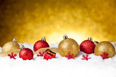 Lots of colorful Christmas Decoration baubles in snow on golden backgroundの写真素材