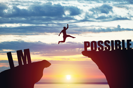 Man jumping over impossible or possible over cliff on sunset backgroundの写真素材