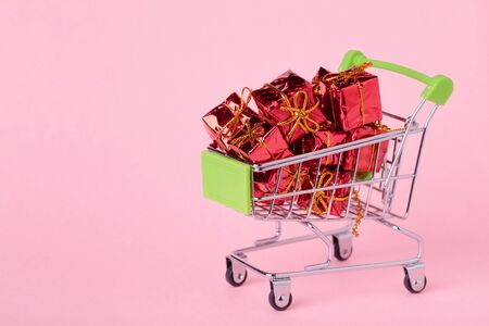 Christmas gifts in a supermarket trolley on pink background. Online shopping concept - trolley full of gifts.の写真素材