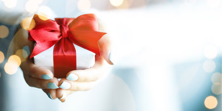 Hands holding little gift with red bow. Close up.の写真素材