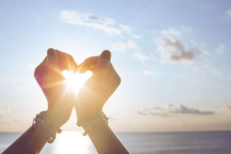 Heart shape making of hands against blue sky and sunの写真素材