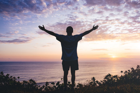 Man with arms outstretched celebrating in beautiful inspiring sunset