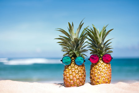 Creative tropical pineapple pair in sunglasses on sandy beachの写真素材