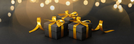 Black gift box with golden ribbon bow on black background.の写真素材