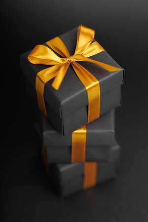 Black gift box with golden ribbon bow on black background.の写真素材