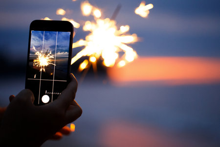 Beautiful sparklers and smartphone on the beach in the sunsetの写真素材