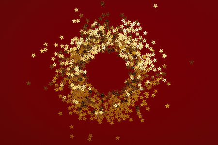 A beautiful wreath crafted from shiny gold stars set against a vibrant red background, creating a stunning visual effectの写真素材