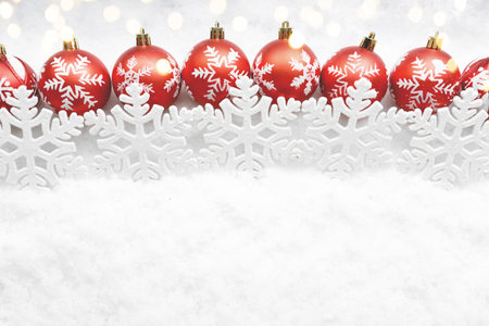 A beautiful and vibrant row of red Christmas balls accompanied by delicate snowflakes set against a crisp white background, creating a festive atmosphereの写真素材