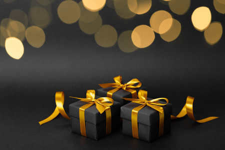 There are three elegant black gift boxes adorned with shiny gold ribbons, all beautifully displayed on a dark black background to highlight themの写真素材