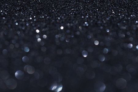 The image features a stark black background that is embellished with a significant amount of sparkling glitter scattered across the surfaceの写真素材