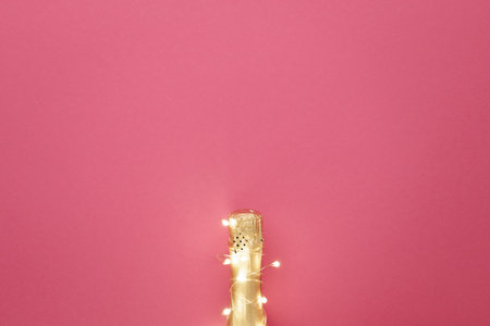 A beautiful and festive bottle of champagne adorned with sparkling Christmas lights is set against a soft pink background, creating a whimsical atmosphereの写真素材