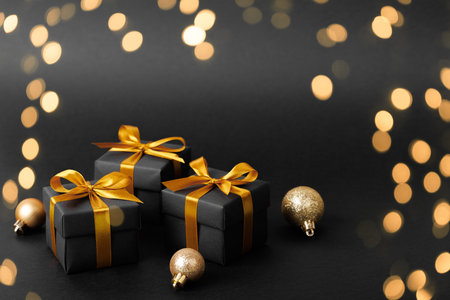 There are three elegant black gifts adorned with beautiful gold bows and ribbons, all displayed against a dark black backgroundの写真素材