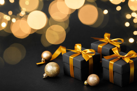 Black gift box with golden ribbon bow on black backgroundの写真素材