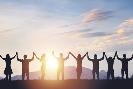 Silhouette of people holding hands against sunset background, concept of peace and victory.の写真素材