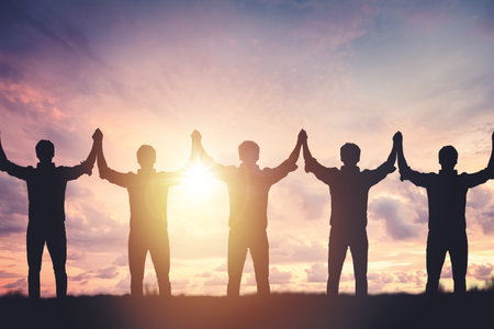 Silhouette of people holding hands against sunset background, concept of peace and victoryの写真素材