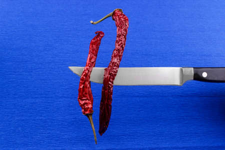 Red hot peppers on a knife on a blue background