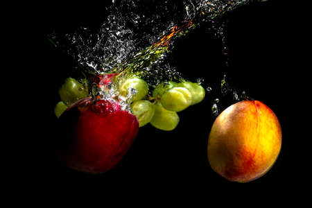 Fruits and grapes falling into the water with splashes and bubblesの写真素材