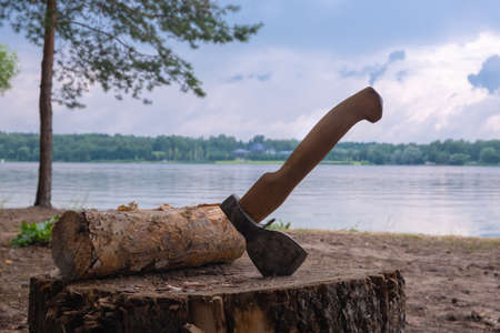 Axe in a log against the background of the river and cloudsの写真素材
