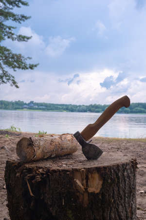 Axe in a log against the background of the river and clouds vertical shootingの写真素材