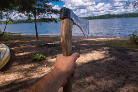 Hand holding an axe against the background of the river and cloudsの写真素材