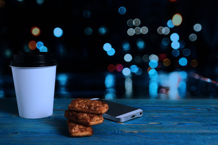 Paper coffee cup, biscuits and telephone on a wooden tableの写真素材