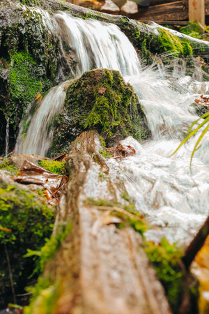 A beautiful waterfall is elegantly surrounded by mossy rocks and a log nearby