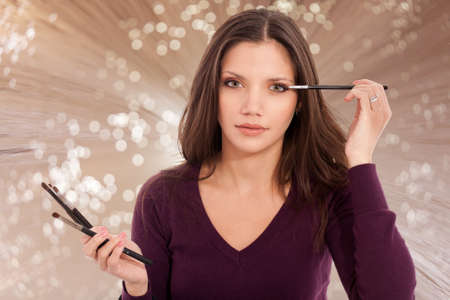 portrait of a beautiful young woman, applying make-up with her brushの写真素材