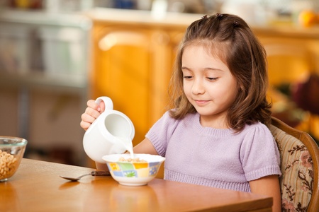little girl having breakfast:pouring milk in the bowlの写真素材