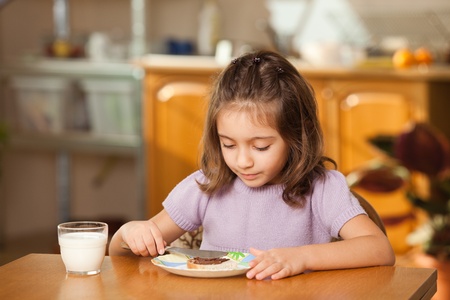 little girl having breakfast: spreading chocolate cream on a slice of breadの写真素材