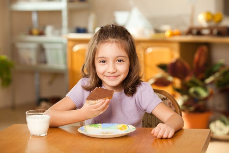 little girl having breakfast: eating chocolate cream on a slice of breadの写真素材
