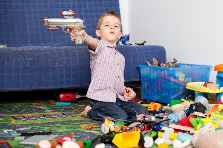 A five year old child playing in his room with a lot of toys around him  A five year old boy pointing at something someone with his toy gunの写真素材