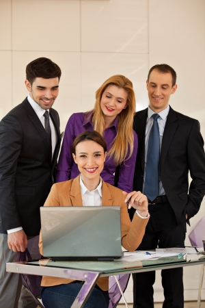 Young beautiful business woman smiling with a laptop in front of her and three colleagues business people in the backの写真素材