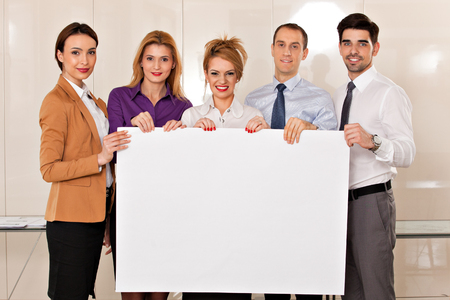 team of young business people, two men and three women,  holding a white cardboardの写真素材