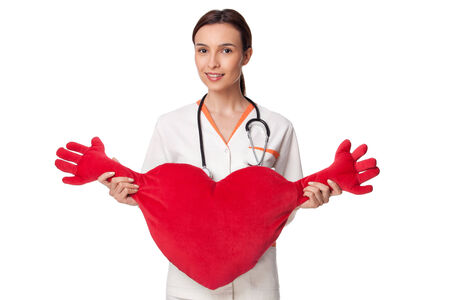creative photo of a nurse or medicine student holding a big heart with hands; beautiful young doctor with stethoscope, wearing white uniform, isolated on white backgroundの写真素材